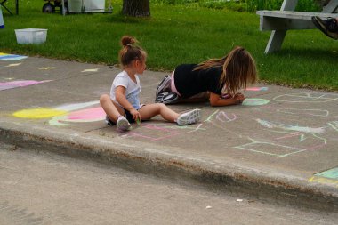 Fond du Lac, Wisconsin USA - 7 Haziran 2025: Çocuklar ve yetişkinler kaldırımları halk parkındaki resimlerle renklendirmek için renkli tebeşir kullanıyorlar.