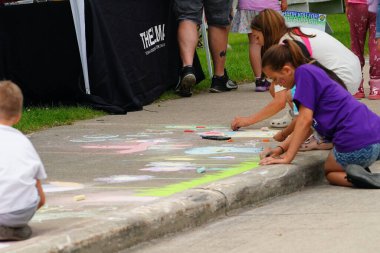 Fond du Lac, Wisconsin USA - 7 Haziran 2025: Kızlar ve erkekler kaldırımları halk parkındaki resimlerle renklendirmek için renkli tebeşir kullanıyorlar.