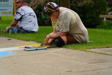 Fond du Lac, Wisconsin USA - 7 Haziran 2025: Genç kızlar kaldırımları halk parkındaki resimlerle renklendirmek için renkli tebeşir kullanıyorlar.