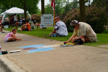 Fond du Lac, Wisconsin USA - 7 Haziran 2025: Çocuklar ve yetişkinler kaldırımları halk parkındaki resimlerle renklendirmek için renkli tebeşir kullanıyorlar.