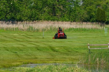 New Lisbon, Wisconsin USA - May 23rd, 2025: Man using riding lawn mower to cut their grass on their property yard.