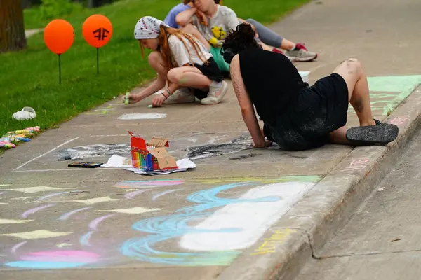 Fond du Lac, Wisconsin USA - 7 Haziran 2025: Çocuklar ve yetişkinler kaldırımları halk parkındaki resimlerle renklendirmek için renkli tebeşir kullanıyorlar.