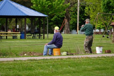 Tomah, Wisconsin ABD - 28 Mayıs 2025: İki yaşlı adam birlikte bir gölde balık tutuyorlar.