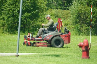 Fond du Lac, Wisconsin USA - July 22nd, 2025: Man cutting grass on a zero turn sit down lawnmower.