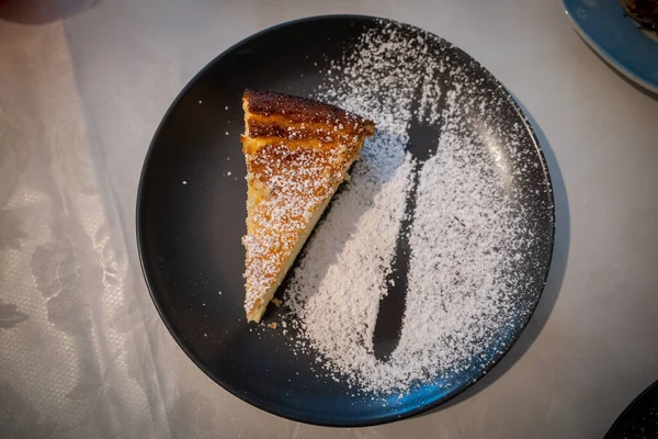 on a plate is a piece of cheesecake with powdered sugar decoration