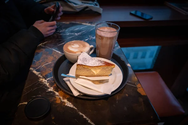 Stock image on the table there is a piece of cheesecake, a glass of cocoa and a cup of cappuccino 