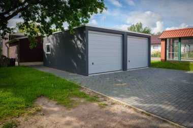 Yeni yapılmış çift katlı garaj. Tekerlekli kapılar bir ağacın altında duruyor.