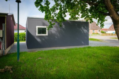 Yeni yapılmış çift katlı garaj. Tekerlekli kapılar bir ağacın altında duruyor.