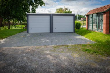 Yeni yapılmış çift katlı garaj. Tekerlekli kapılar bir ağacın altında duruyor.