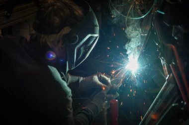 Kaynak maskesi takan biri kaynak makinesiyle metalle çalışır ve kaynak işlemi sırasında kıvılcımlar yaratır.