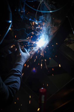 Kaynak maskesi takan biri kaynak makinesiyle metalle çalışır ve kaynak işlemi sırasında kıvılcımlar yaratır.