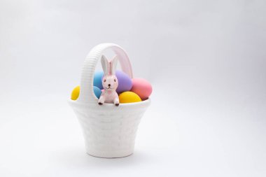 Mutlu Paskalyalar, beyaz seramik sepette süslenmiş yumurtalarla duran tavşan. Yiyici Şenlikli Tavşan ve renkli Paskalya yumurtaları, beyaz arka planda fotokopi alanı ile izole edilmiş.