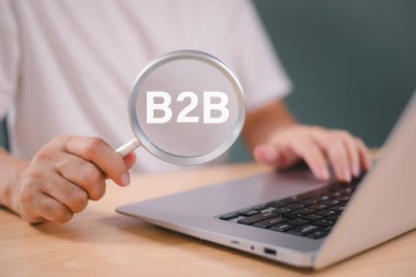 B2B e-ticaret pazarlama konsepti. İşadamı, şirket işbirliği ve eylem planı stratejisi için cam araştırma B2B simgesini büyütmek üzere bilgisayar yazılımı kullanıyor. İş dünyasından ticaret teknolojisine
