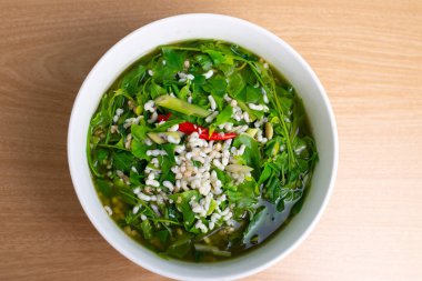 Thai food Melientha suavis plant in soup with red ant egg. Famous green leaves food in white bowl on wooden table, top view background. Local ingredient vegetable, red ant eggs, topview clipart