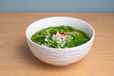 Thai food Melientha suavis plant in soup with red ant egg. Famous green leaves food in white bowl on wooden table, top view background. Local ingredient vegetable, red ant eggs, savory dish style clipart