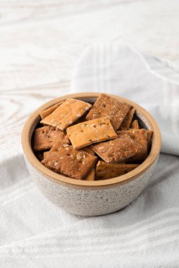 Bir kase kuru kraker, domates ve fesleğen, ahşap kaplama ve peçeteli..