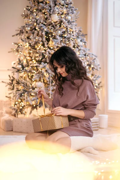 On Christmas days a beautiful woman opens her gift under the Christmas tree. Concept of: magic, christmas, gift, holidays