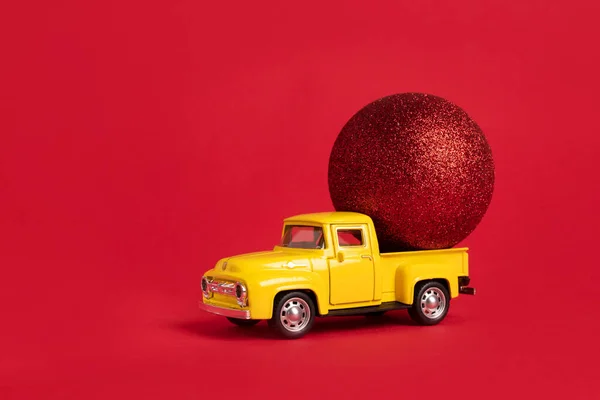 Yellow retro toy pickup carrying a red balls on red background. Christmas and New Year celebration concept. Copy space