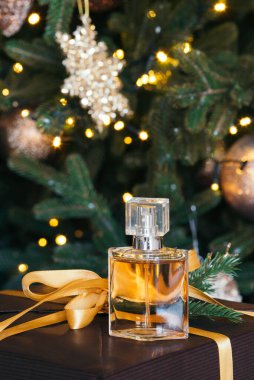 Bir Noel ağacının arka planında cam bir masada duran güzel hediye edilmiş kadın parfümü şişesi. Yeni yıl hediyesi, çelenk ışıkları, oyuncaklar ve tatil konsepti..
