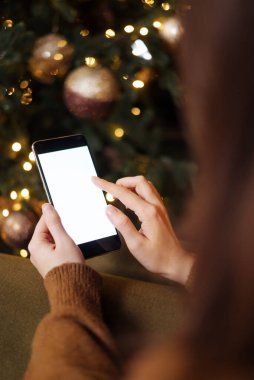 Mesaj atmak için yeri olan bir Noel modeli. Noel reklamı, uygulama şablonu. Telefonun arkasında boş bir ekran olan el ele tutuşmuş altın gibi güzel bir Noel ağacının akşam ışıkları altında..