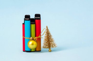 Renkli tek kullanımlık elektronik sigaralar yılbaşı hediyesi olarak mavi arka planda Noel ağacı ile birlikte paketlenir. Modern sigara konsepti.