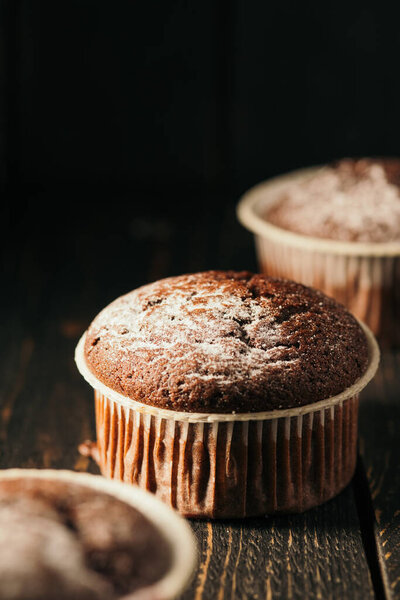 Chocolate muffins with powdered sugar on a black background. Still life close up. Dark moody. Food photo