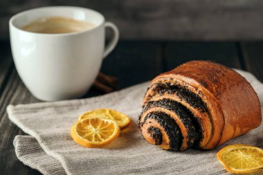 Haşhaş tohumlu çörekler ve koyu ahşap arka planda peçeteli bir fincan kahve..