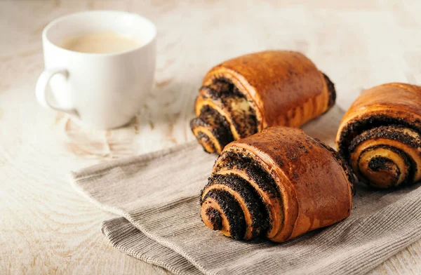 buns with poppy seeds and a cup of coffee on light wood background.