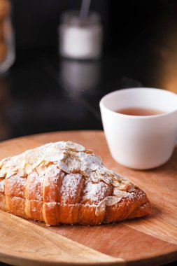 Tahta tezgahta pudralı taze kruvasan ve koyu arkaplanda bir fincan çay..