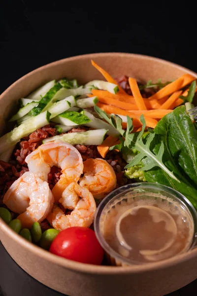 stock image Bowl with shrimps, carrots, cucumbers, beans and vegetables with herbs, on a black background. Healthy food concept