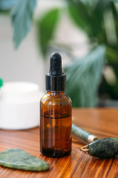 Essential aroma oil or serum essence in glass bottle on a wooden table against a background of green plants and beauty products. Concept of cosmetology, medicine