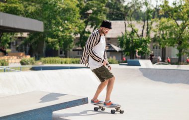 Şık bir yetişkin adam kaykay parkının rampasında kaykay sürüyor. Güneşli bir günde paten parkında kaykay antrenmanı yapmak.