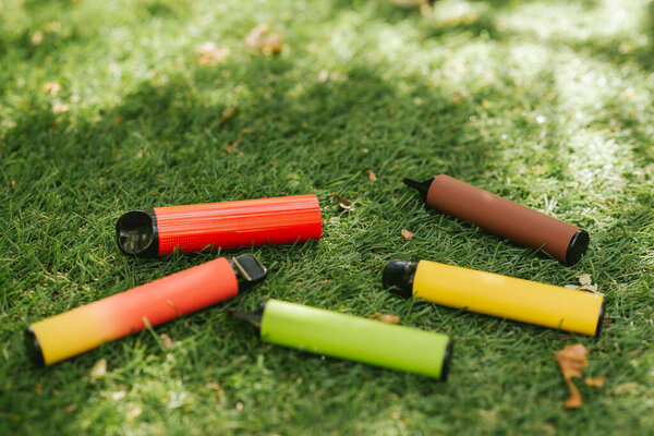 Vaping devices. Set of colorful electronic cigarettes. Electronic sticks for vaping on green grass with sun rays