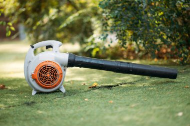 A close-up of an orange cordless, electric leaf blower lying on a grass. Autumn, fall gardening works in a backyard, on a lawn. Garden works.