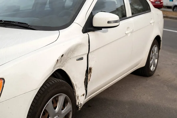 Damaged side door on a white car after a small traffic accident requiring a repair