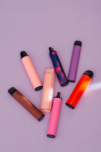 Colorful disposable electronic cigarettes on a purple background. The concept of modern smoking, vaping and nicotine. Top view