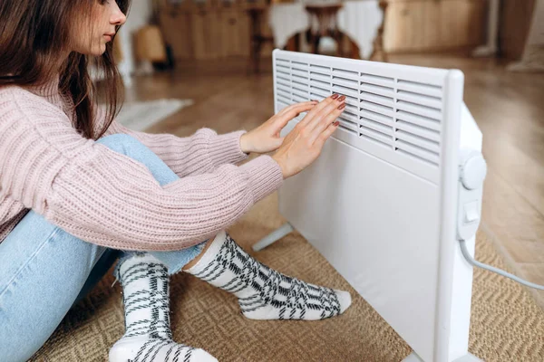 Woman warming hands near electric heater at home. Using heater at home in winter. Woman warming her hands. Heating season. . High quality photo