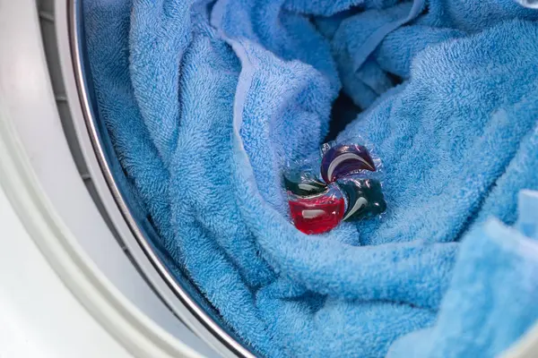 Laundry detergent capsule in washing machine drum on a blue towel