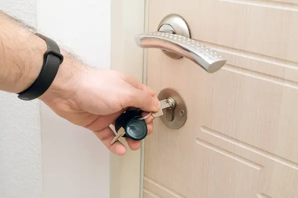 The man unlocks the wooden door in modern house. Caucasian man opens door with his hand. Key on the door. High quality photo