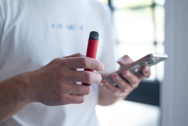 Kyiv, Ukrayna - 2 Mayıs 2024 kırmızı tek kullanımlık elektronik sigara iPhone 15 bir adamın elinde. Modern çevrimiçi iletişim.