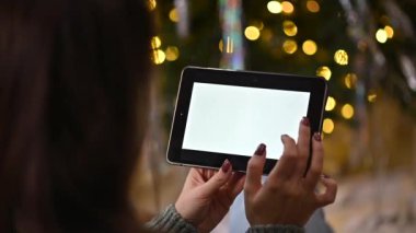 Kadın elleri, süslenmiş Noel ağacında dijital tablet beyaz ekran kullanarak dokunuyor, sörf yapıyor.