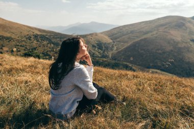 Kadın sırtında dağ tarlasında oturur ve dağlarda gün batımına hayran kalır..