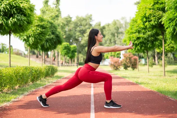 the woman athlete in sports apparel, doing lunges, stretching in the Park. fitness training outdoors. strength exercises, cardio workout.
