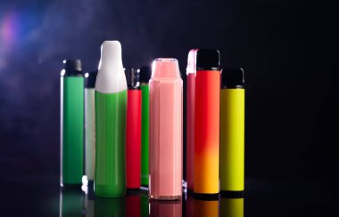 Siyah arka planda dumanlı farklı şekillerde tek kullanımlık renkli elektronik sigaralar. Modern sigara, buhar ve nikotin kavramı..