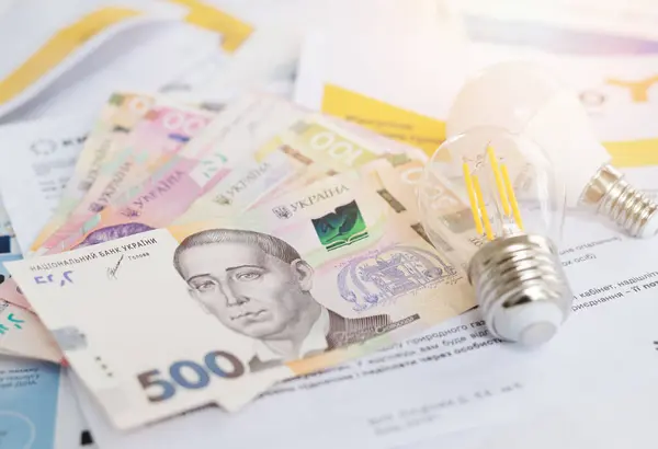 stock image Ukrainian banknotes and light bulbs on utility bills, symbolizing electricity costs and energy expenses. 