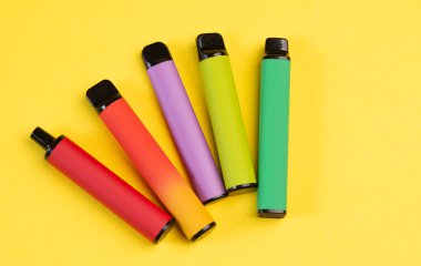 Sarı arka planda tek kullanımlık renkli elektronik sigaraların tasarımı. Modern sigara, buhar ve nikotin kavramı. Üst görünüm. 