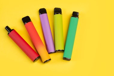 Sarı arka planda tek kullanımlık renkli elektronik sigaraların tasarımı. Modern sigara, buhar ve nikotin kavramı. Üst görünüm. 