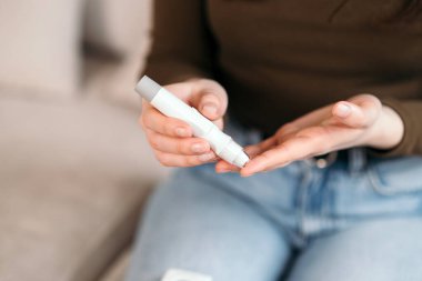 Genç bir kadın evdeki kan şekerini glukometreyle ölçüyor, diyabet hastalığını kanepede izliyor. 