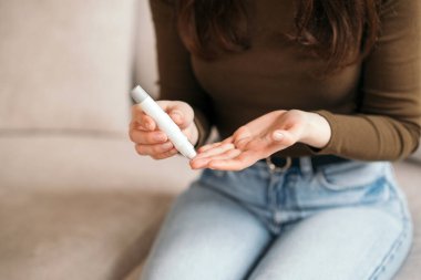 Genç bir kadın evdeki kan şekerini glukometreyle ölçüyor, diyabet hastalığını kanepede izliyor. 