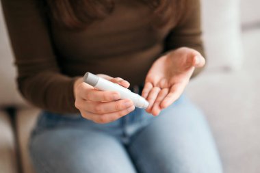 Genç bir kadın evdeki kan şekerini glukometreyle ölçüyor, diyabet hastalığını kanepede izliyor. 